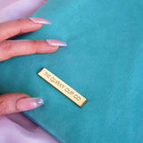 A close-up of the gold metal nameplate engraved with 'THE QUIRKY CUP CO' on the back of the aqua velvet eReader sleeve in Antoinette.