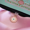 The Antionette dust plug design by The Quirky Cup Collective is plugged into a kindle on a light pink fabric background. The gold dust plug design (as part of the romantasy e-reader decor release) features a floral motif in shades of light pink, mint green and cream.