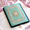 The Antionette Kindle Sticker Insert by The Quirky Cup Collective is attached to a kindle sitting on a book on a light pink fabric background. A sticker to attach directly to your feminine romantasy inspired kindle, the design features a french flower frame motif in shads of gold, pink and cream on the light mint coloured background. The kindle also features a matching Antionette dust plug with the same flower motif.