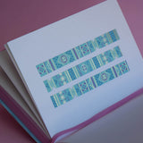 The Aurum washi tape in Antoinette features geometric designs in shades of pink, gold and blue. Three stripes of the tape are in a page of the french inspired notebook against a pink background.
