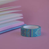 The Aurum design of French inspired washi tape as part of the Antoinette collection sits on a light pink background. The whimsical washi tape features geometric flower motifs in shades of blue, pink and foil gold.