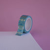 The Aurum design of French inspired washi tape as part of the Antoinette collection sits on a light pink background. The whimsical washi tape features geometric flower motifs in shades of blue, pink and foil gold.