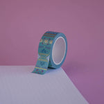 The Aurum design of French inspired washi tape as part of the Antoinette collection sits on a light pink background. The whimsical washi tape features geometric flower motifs in shades of blue, pink and foil gold.