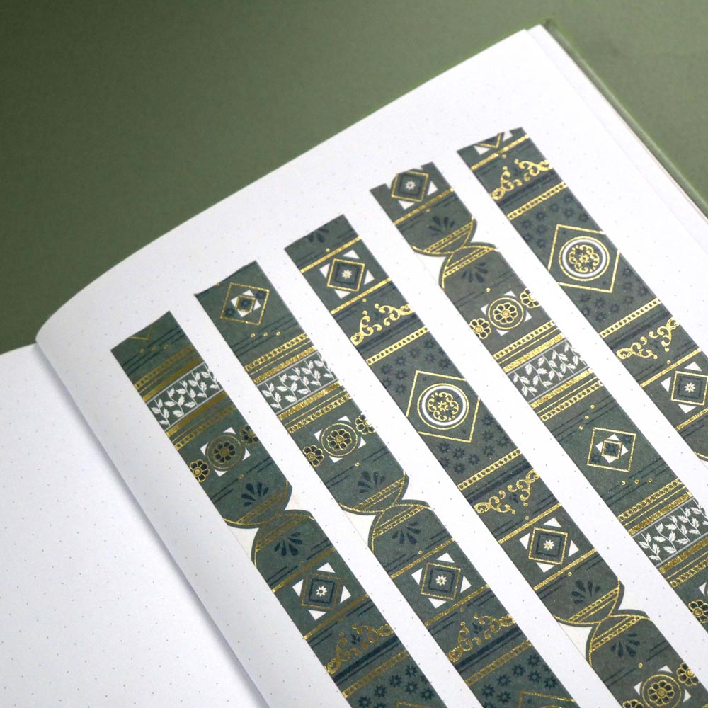 The Sage green variation of the Aurum Literati washi tape. The book inspired washi tape design is shown as 5 strips on a page of a journal on a green background and features a geometric design inspired by classical book ornaments in shades of dark green, sage green and gold.