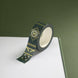 The Sage green variation of the Aurum Literati washi tape. The book inspired washi tape design is shown on the edge of a journal on a green background and features a geometric design inspired by classical book ornaments in shades of dark green, sage green and gold.