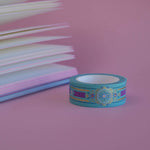 The Balteus design of French inspired washi tape as part of the Antoinette collection sits on a light pink background. The romantasy inspired washi tape features a classical book inspired motif in shades of blue, pink and foil gold.