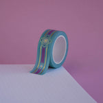 The Balteus design of French inspired washi tape as part of the Antoinette collection sits on a light pink background. The romantasy inspired washi tape features a classical book inspired motif in shades of blue, pink and foil gold.