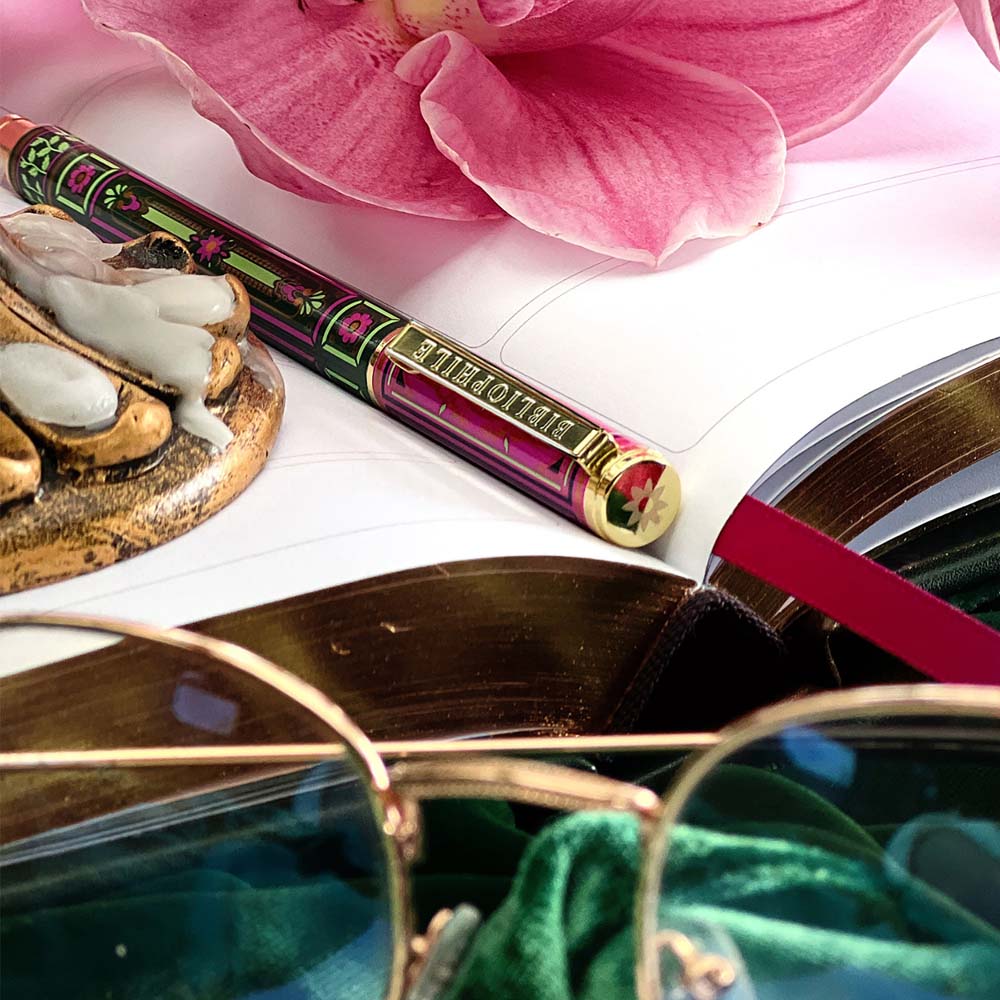 Decorative pen with pink flower, gold object, and open book on a white surface