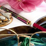 Decorative pen with pink flower, gold object, and open book on a white surface