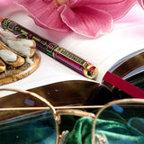 Decorative pen with pink flower, gold object, and open book on a white surface