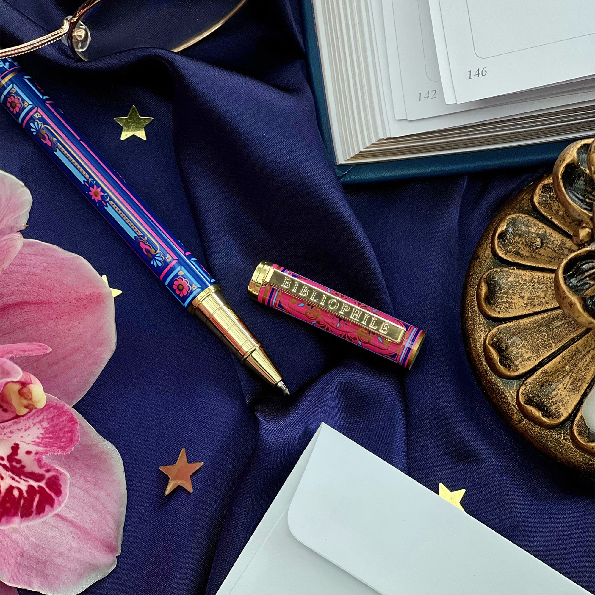 Decorative blue and pink literati pen on a blue fabric background with a book and decorative items.