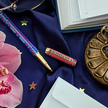 Decorative blue and pink literati pen on a blue fabric background with a book and decorative items.