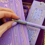 A decorative pen by The Quirky Cup Collective shows an intricate victorian inspired design in shades of pastel pink and purple and the phrase 'Bibliophile' engraved on the clip. The pen sits on a matching wisteria reading journal and bookmark.