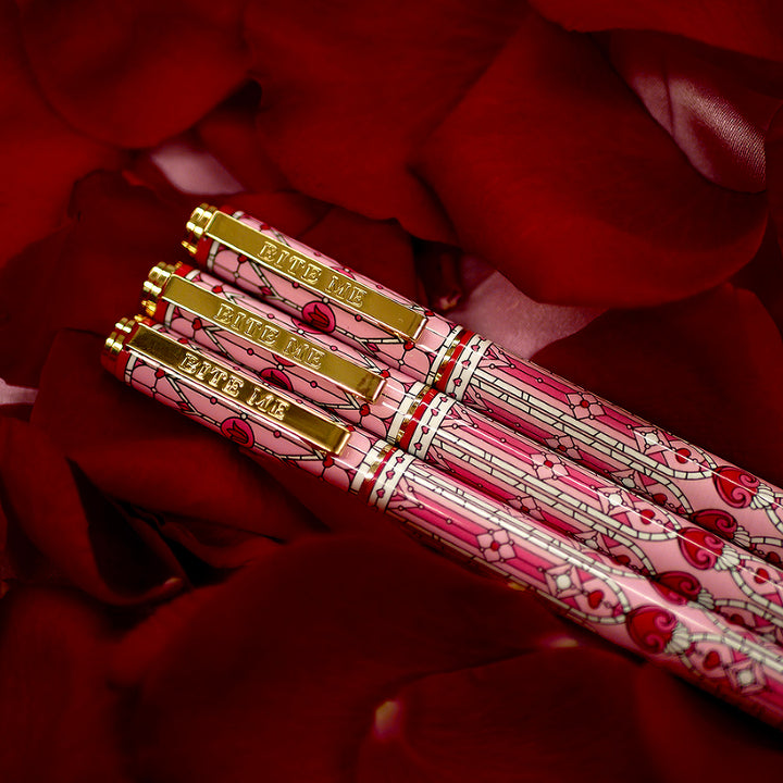 Bite Me Pen- The Quirky Cup Collective - Stained Glass Inspired Pen Design with 'Bite me' engraved on the pen clip. Pen sits on a bed of red rose petals. 