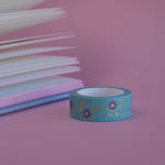 The Botanica design of French inspired washi tape as part of the Antoinette collection sits on a light pink background. The bookish washi tape design features flowers on a vibe in shades of pink and foil gold.