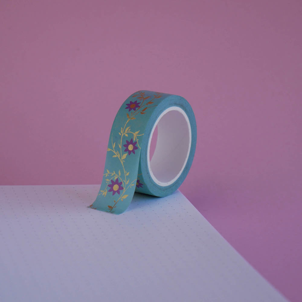 The Botanica design of French inspired washi tape as part of the Antoinette collection sits on a light pink background. The bookish washi tape design features flowers on a vibe in shades of pink and foil gold.