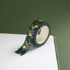 The Sage green variation of the Botanica Literati washi tape. The classic book inspired washi tape design is shown on the edge of a journal page on a green background and features a a vine covered in tiny flowers and leaves in shades of dark green, sage green, white and foiled gold.