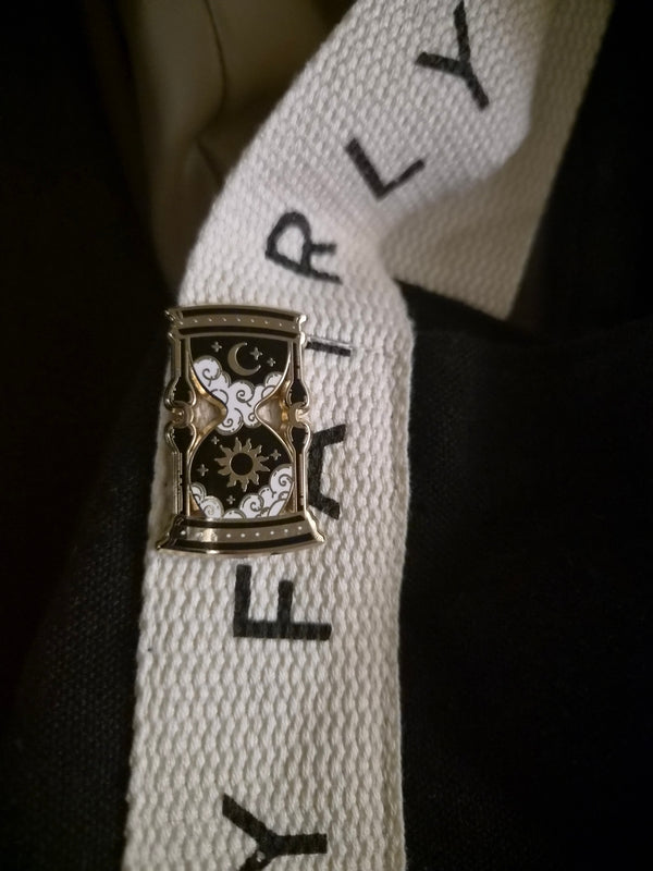 A dark fantasy enamel pin design of a hourglass on a lanyard
