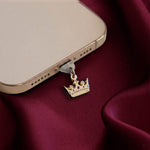 An detail shot of the gold Gilded Heir dust plug in a phone on a deep red fabric background. The fantasy aesthetic kindle decor sees the dust plug feature a small crown motif with red details.
