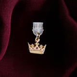 An detail shot of the gold Gilded Heir dust plug on a deep red fabric background. The fantasy aesthetic kindle decor sees the dust plug feature a small crown motif with red details.