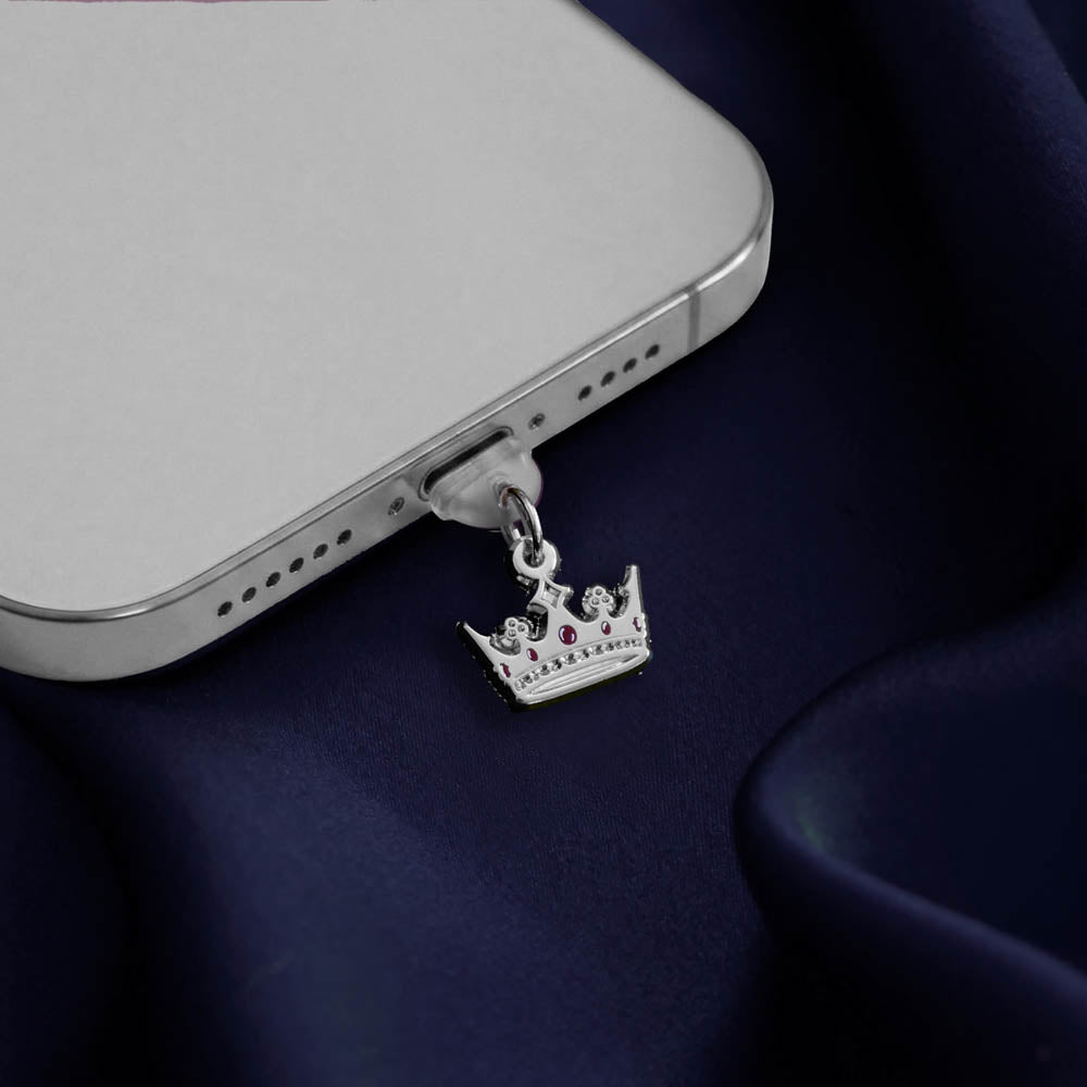 An detail shot of the silver Gilded Heir dust plug in a phone on a deep blue fabric background. The fantasy aesthetic kindle decor sees the dust plug feature a small crown motif with red details.
