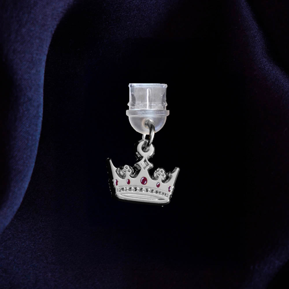 An detail shot of the silver Gilded Heir dust plug on a deep blue fabric background. The fantasy aesthetic kindle decor sees the dust plug feature a small crown motif with red details.