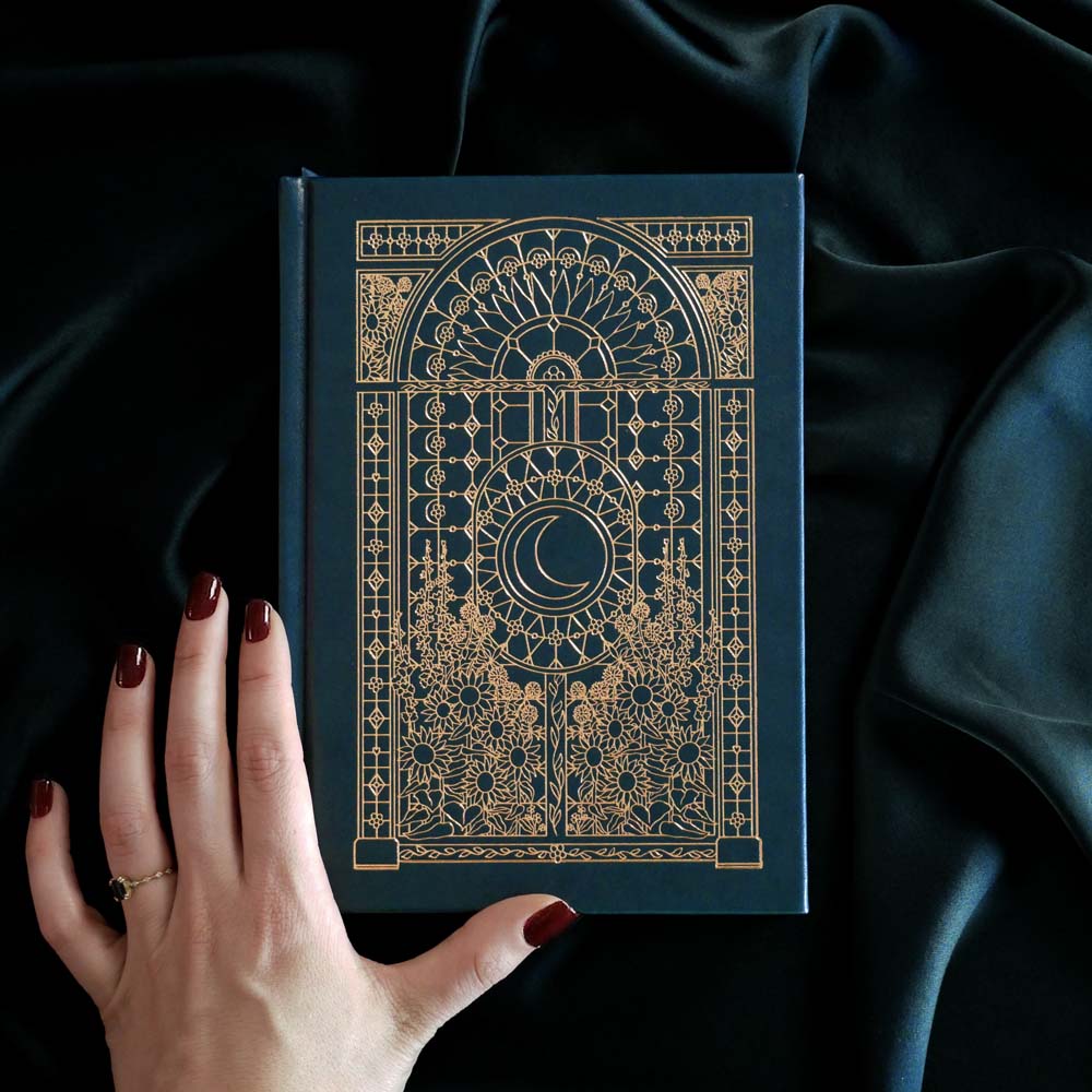 Decorative dateless planner with gold embossed design held by a hand against a dark fabric background