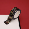 A close up of the Dragon Born washi tape by The Quirky Cup Collective. The roll of fantasy inspired washi tape is on the corner of a white journal on a red background. The bookish washi tape design is red and black with gold detailing- the intricate design showing a serpent eye.
