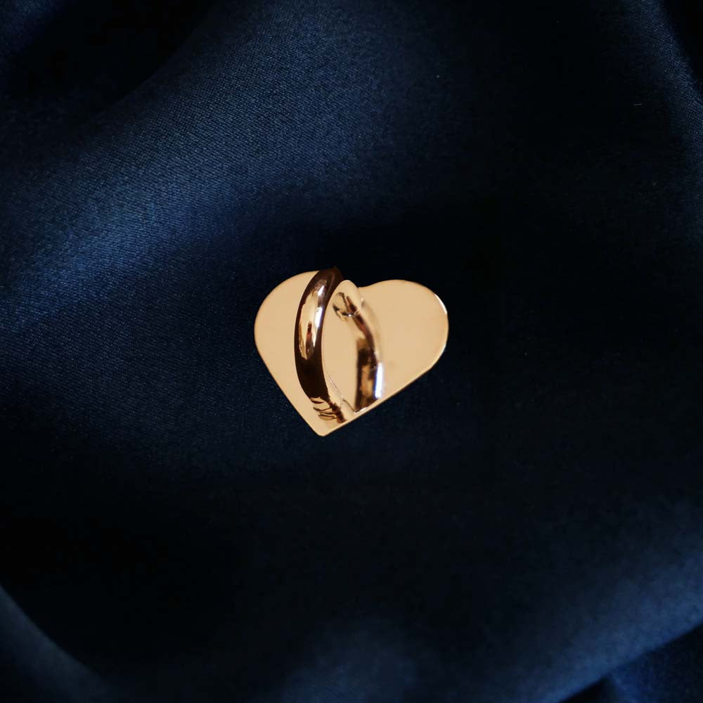 A The Quirky Cup Collective charm anchor on a dark blue fabric background. The gold heart-shaped clip is used to attach Charmlets to flat surfaces (such as your device).
