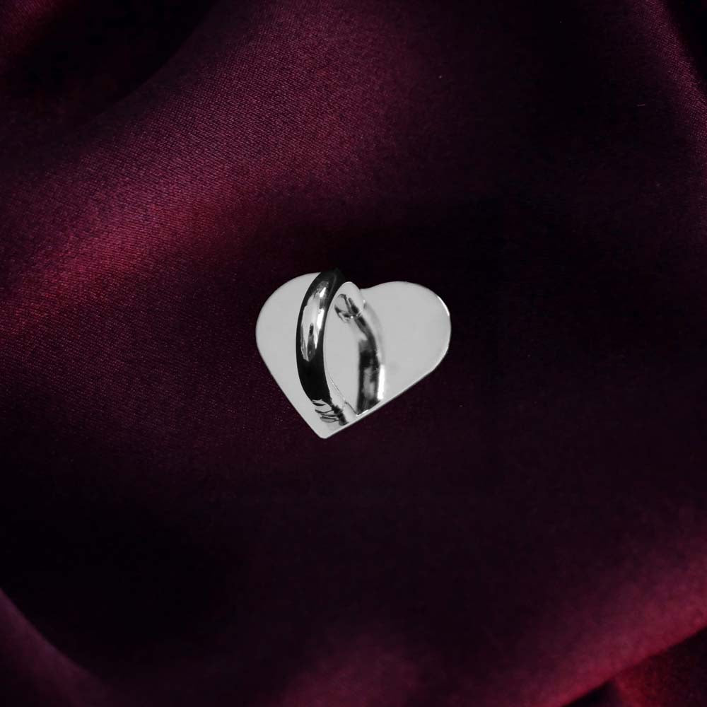 A The Quirky Cup Collective charm anchor on a dark burgundy fabric background. The silver heart-shaped clip is used to attach Charmlets to flat surfaces (such as your device).