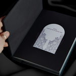 black journal sits open on background of black draped silk. On the front end page it says 'the adventures of' to show where you can write your name
