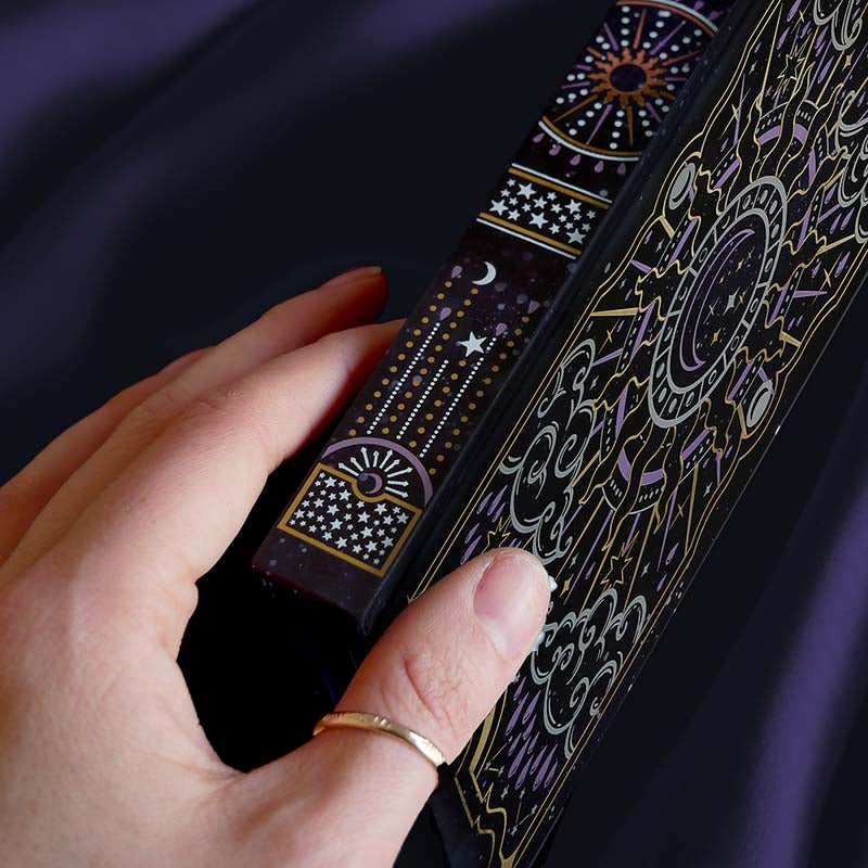 Celestial Journal with celestial spine sits on a purple silky background with a hand caressing the spine.