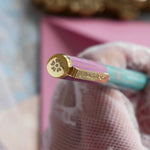 A detail of the L'amour L'emporte pen in shows the floral motif etched in the top of the cap. The french inspired gel pen features floral motifs inspired by a classic literature aesthetic and 'L'AMOUR L'EMPORTE' etched into the pen clip.