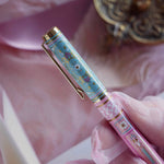 A detail of the Bibliophile pen in the pastel pink and aqua Antoinette colour-way. The french inspired gel pen features floral motifs inspired by a classic literature aesthetic and 'BIBLIOPHILE' etched into the pen clip.