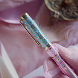 A detail of the Bibliophile pen in the pastel pink and aqua Antoinette colour-way. The french inspired gel pen features floral motifs inspired by a classic literature aesthetic and 'BIBLIOPHILE' etched into the pen clip.