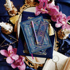 An overhead shot the blue literati bundle- a blue leather notebook with intricate gold foil detailing, accompanied by a matching blue pen, a bookmark, and a plush velvet book sleeve, all displayed on a surface with decorative elements like flowers and gold trim.