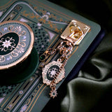 The Sage Literati clingie is a gold oval shaped eReader grip with green and gold floral motif design. The kindle grip (similar to an enamel pop socket) is attached to an eReader with a matching green sticker insert and a gold and green Charmlet  all sitting on a sage green background.