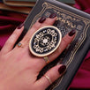 Hand holding a round, decorative clingie MagSafe device grip with intricate designs against a black fabric background.