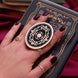 Hand holding a round, decorative clingie MagSafe device grip with intricate designs against a black fabric background.