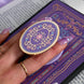 The back of a kindle shows the wisteria light purple literati eReader sticker insert alongside matching oval clingie. Both are light purple and feature pastel pink, purple and blue detailing alongside the gold enamel and foil. The products feature classical Victorian book inspired motifs and the kindle is held in front of a classical book.