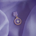 An detail shot of the wisteria literati dust plug on a light purple fabric background. The dust plug is light purple with a gold and white flower design in a circle shape.
