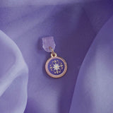 An detail shot of the wisteria literati dust plug on a light purple fabric background. The dust plug is light purple with a gold and white flower design in a circle shape.