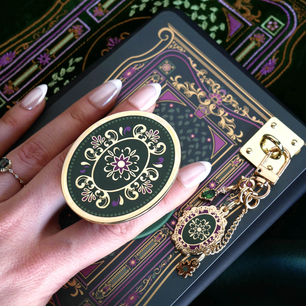 The detail of the forest green literati eReader decor bundle. The classic book inspired kindle set-up includes a charmlet, clingie, eReader sleeve, dust plug and eReader sticker insert all in shades of black, green and purple with designs inspired by classic literary aesthetic. 
