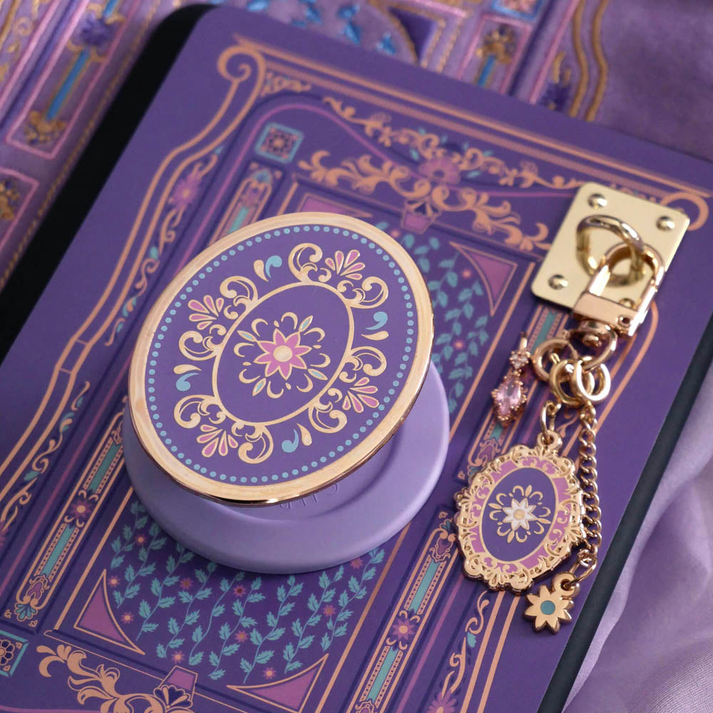 An detail shot of the wisteria literati eReader decor bundle. The set features an eReader sleeve, eReader sticker insert, charmlet and dust plug all in the same light purple colour with pastel pink, purple and blue detailing alongside gold foil and embroidery.