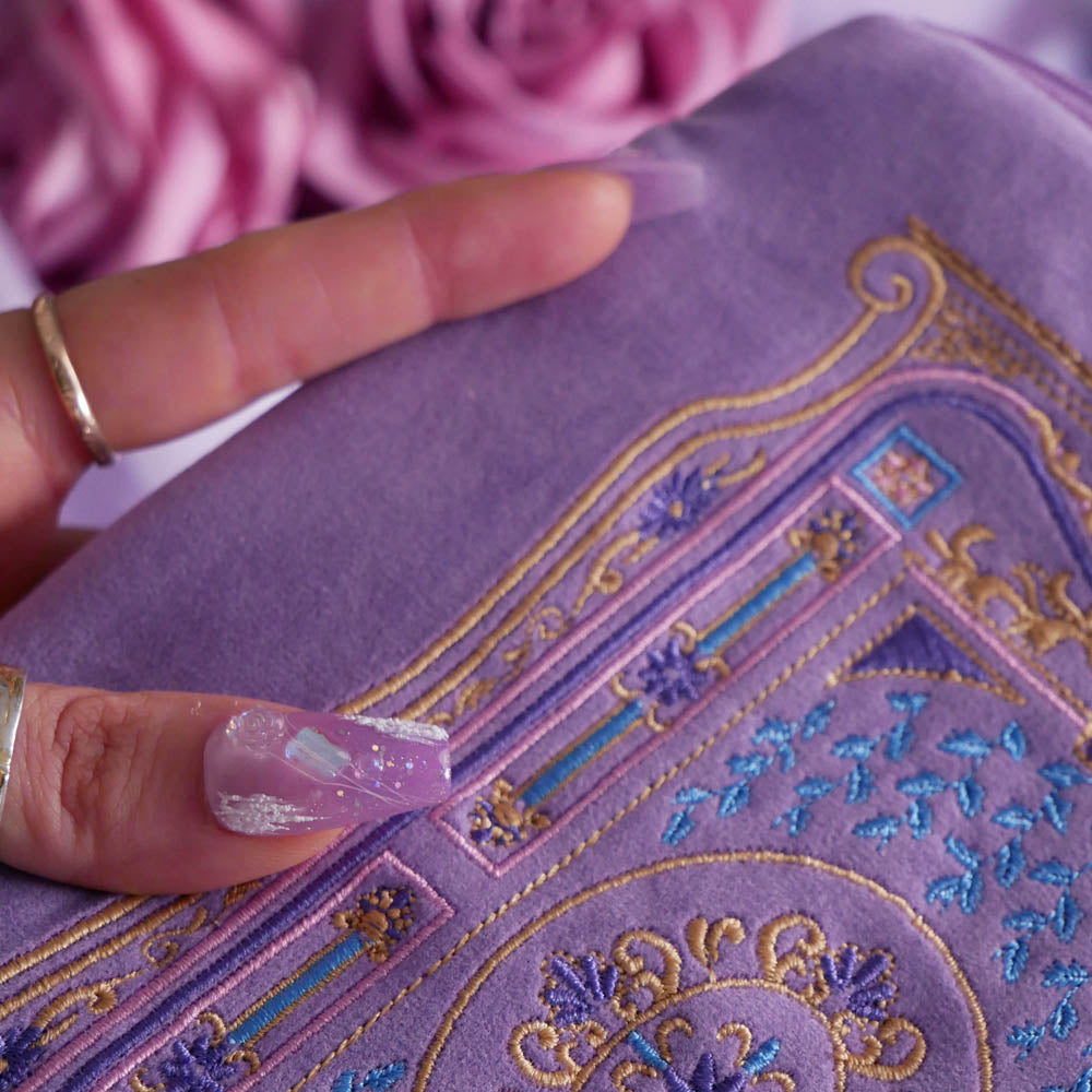 A detail of the intricate embroidery detail on the lilac Literati eReader sleeve in Wisteria. The velvet kindle case features a classical design inspired by victorian classical books with detailed embroidery in shades of blue, purple and gold. 