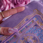 A detail of the intricate embroidery detail on the lilac Literati eReader sleeve in Wisteria. The velvet kindle case features a classical design inspired by victorian classical books with detailed embroidery in shades of blue, purple and gold. 