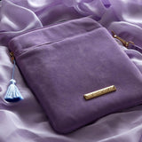A detail of the back of the lilac Literati eReader sleeve in Wisteria. The velvet kindle case features a classical design inspired by victorian classical books with detailed embroidery in shades of blue, purple and gold. The back of the case shows the gold logo plate, the zipper on the back, a light blue tassel and a wrist strap.