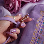 A detail of the lilac Literati eReader sleeve in Wisteria and it's wrist strap. The velvet kindle case features a classical design inspired by victorian classical books with detailed embroidery in shades of blue, purple and gold. The wrist strap is in the same colour and feature gold hardware detailing.