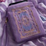 The lilac Literati eReader sleeve in Wisteria sits on a light purple fabric background. The velvet kindle case features a classical design inspired by victorian classical books with detailed embroidery in shades of blue, purple and gold. The case also features a wrist strap and a red light blue tassel.
