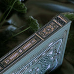 The spine of the sage green Literati Journal shows the intricate gold, green and white design that is foiled. The geometric floral design is inspired by classical books and a love of reading. The book sits on a sage green fabric background surrounded by flowers.